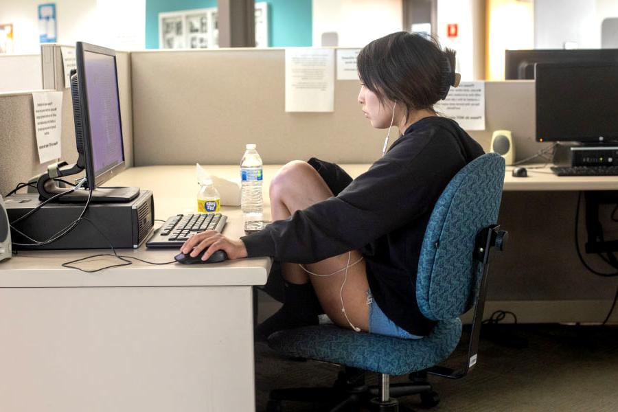 Female student sitting at desk with earbuds in working on caomputer